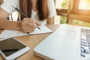 A lady sitting at a desk writing in a notebook with a pencil