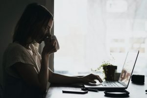 A lady drinking from a cup while looking at her laptop