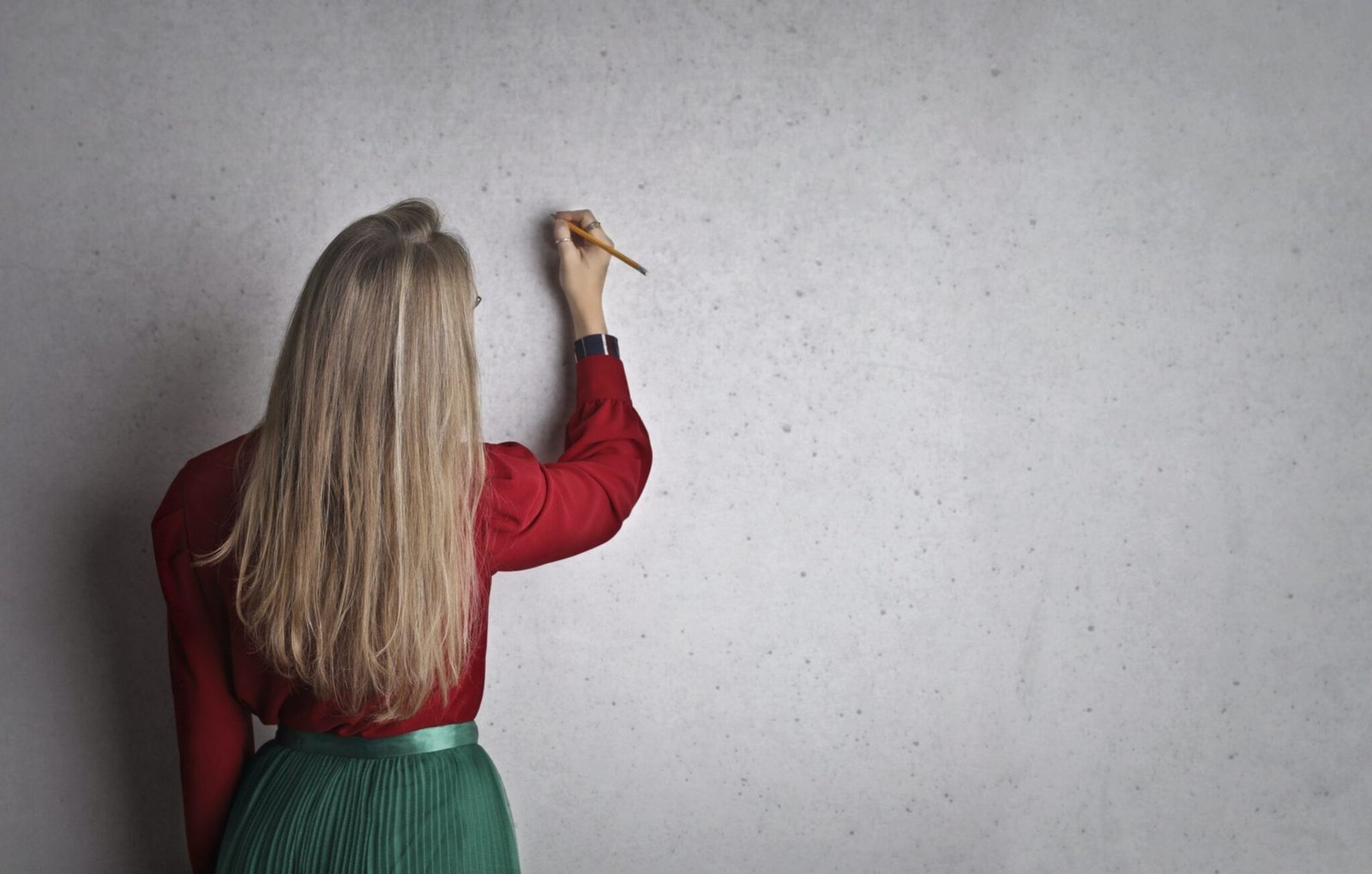 A lady writing notes on a concrete wall with a pencil