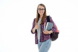 A young student holding books, carrying a backpack and holding her thumb up