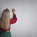A lady writing notes on a concrete wall with a pencil
